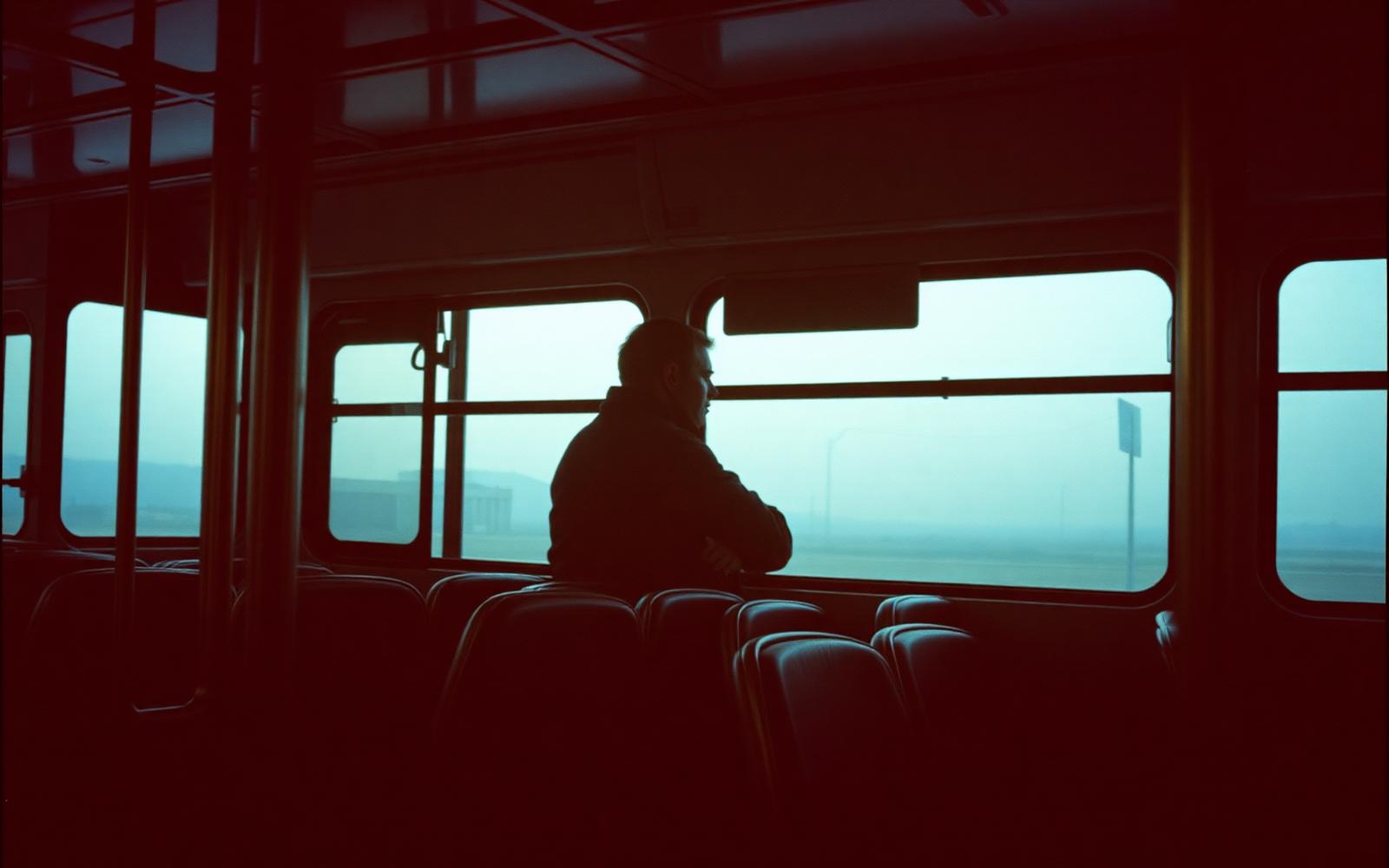 A lone passenger looks out the window of a nearly empty city bus at dusk.
